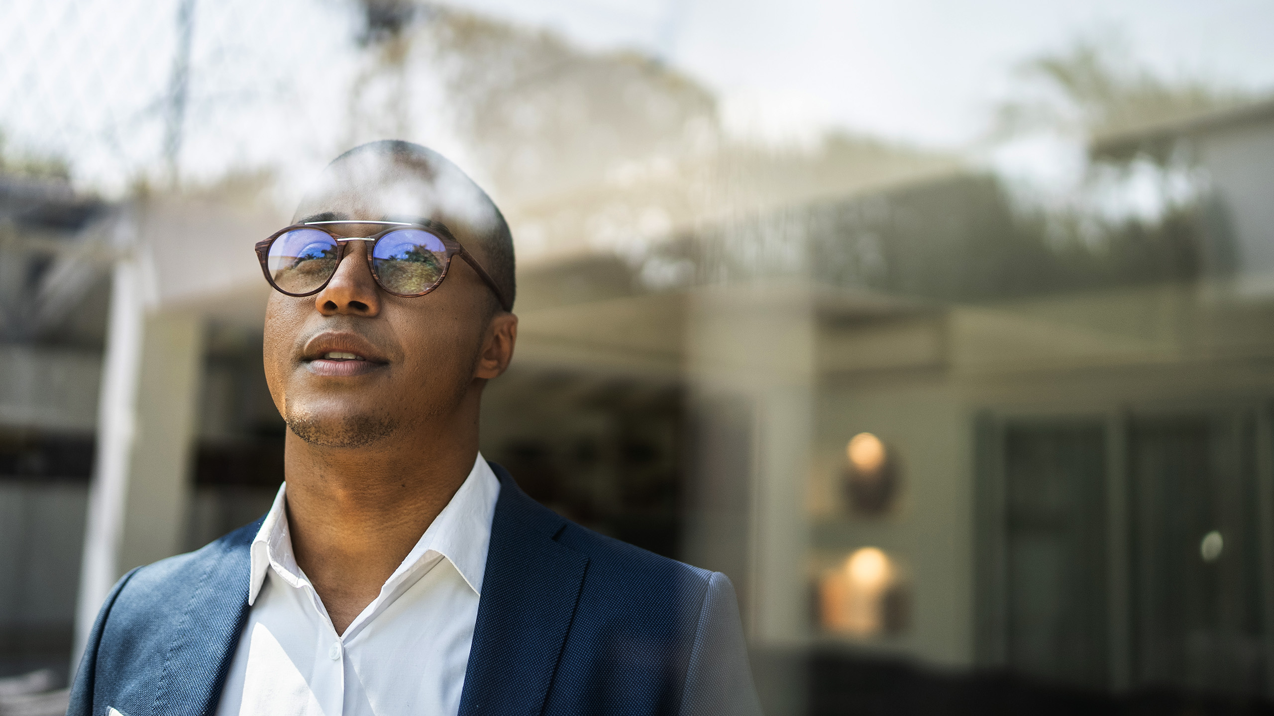 Person wearing professional clothing standing outdoors near a window, with reflections of the surroundings visible on the glass.